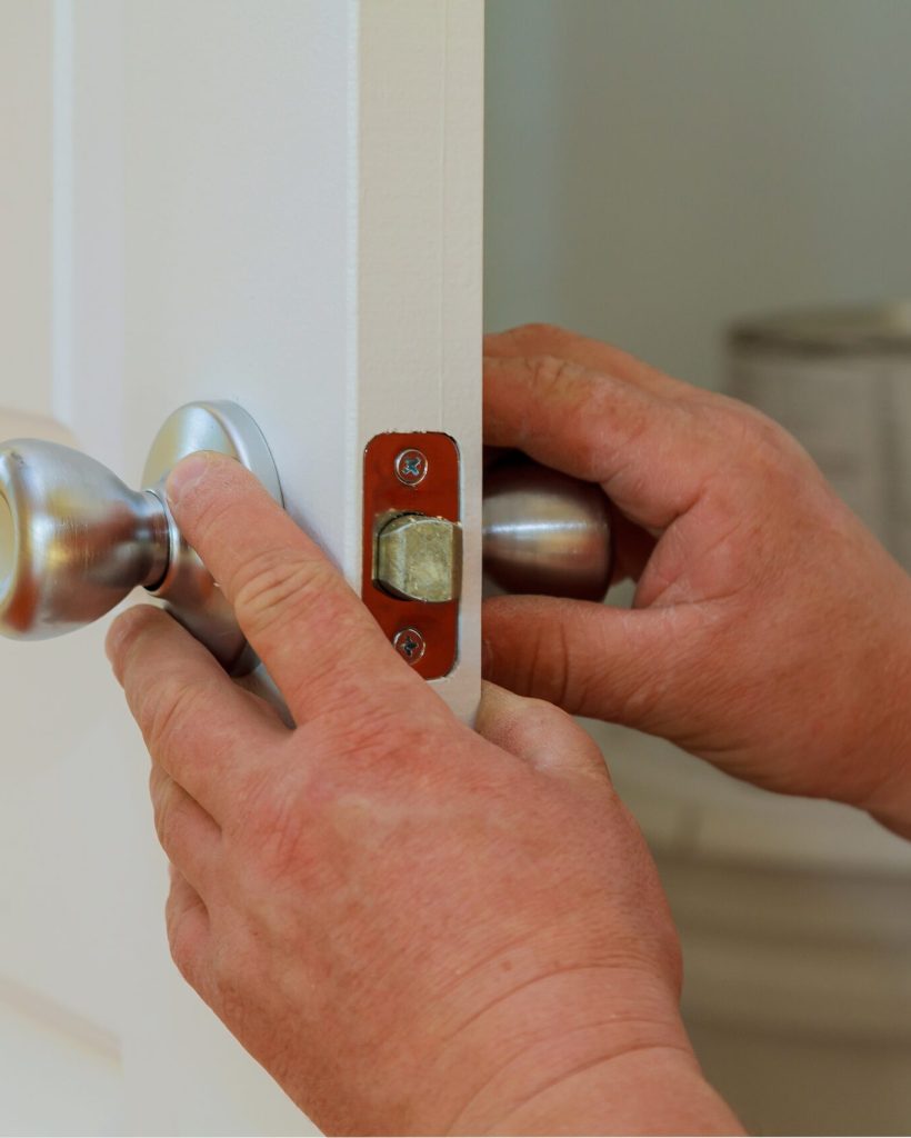 Closeup of a professional locksmith installing or repairing a new deadbolt lock on a house door with the inside internal parts of the lock visible.